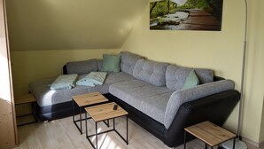 A modern living room with a grey sofa, two wooden side tables, a floor lamp, and a painting of a forest scene.