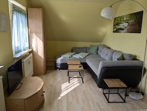 A compact living space with a sofa, a small table, a bench, a TV, and a lamp.