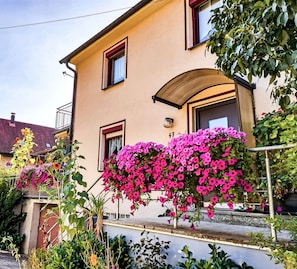 A two-story building with a balcony, a door with a glass panel, and a small window with a curtain. - Vacation Home "Ulbrich" with Private Terrace, Balcony & Wi-Fi (Neudrossenfeld)