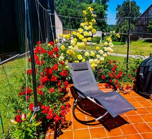 Eine Liege auf einer gefliesten Terrasse, umgeben von farbenprächtigen Blumen.