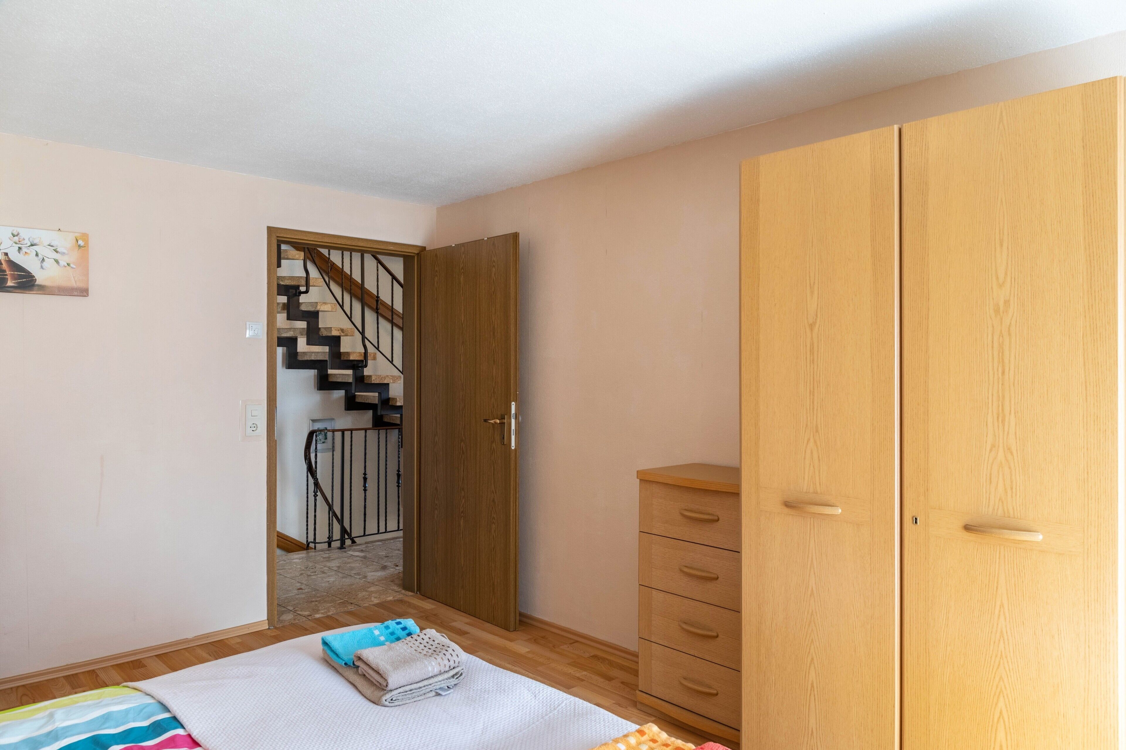 Ein Schlafzimmer mit einem Holzschrank, einem Bett mit gestreifter Decke, einem kleinen Nachttisch und einer Treppe, die in einen anderen Raum führt.