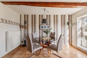 Un área de comedor con una mesa redonda de vidrio, cuatro sillas grises, una lámpara colgante y papel tapiz a rayas.