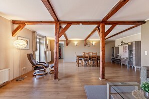 A spacious living area with wooden beams, a dining table, chairs, a sofa, and a television. - Apartment 'Ferienwohnung Obenauf' with Private Terrace and Wi-Fi (Oesterwurth)