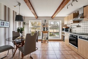 Una cocina moderna con vigas de madera, una mesa de comedor de vidrio y vistas amplias a través de grandes ventanales.