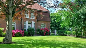 A brick building with a red roof, surrounded by well-maintained grass and flowering bushes. - Apartment 'Ferienwohnung Obenauf' with Private Terrace and Wi-Fi (Oesterwurth)