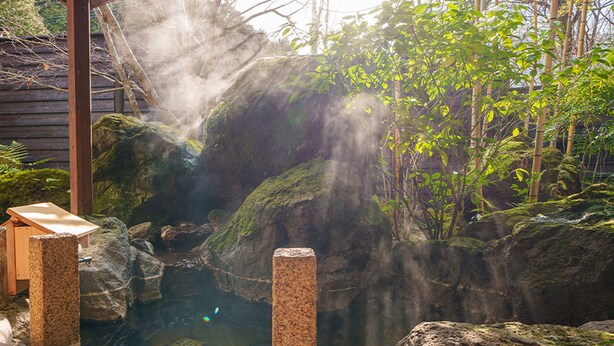 Un área de aguas termales con un banco de madera, rocas y plantas de bambú.