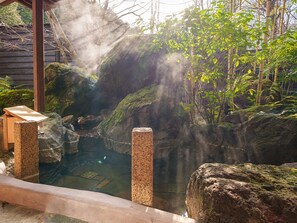 A hot spring area with a wooden bench, rocks, and bamboo plants. - Yufuin Rakuyu (Yufu)