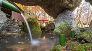 Formación rocosa natural con una cascada pequeña, un estanque y rocas cubiertas de musgo.