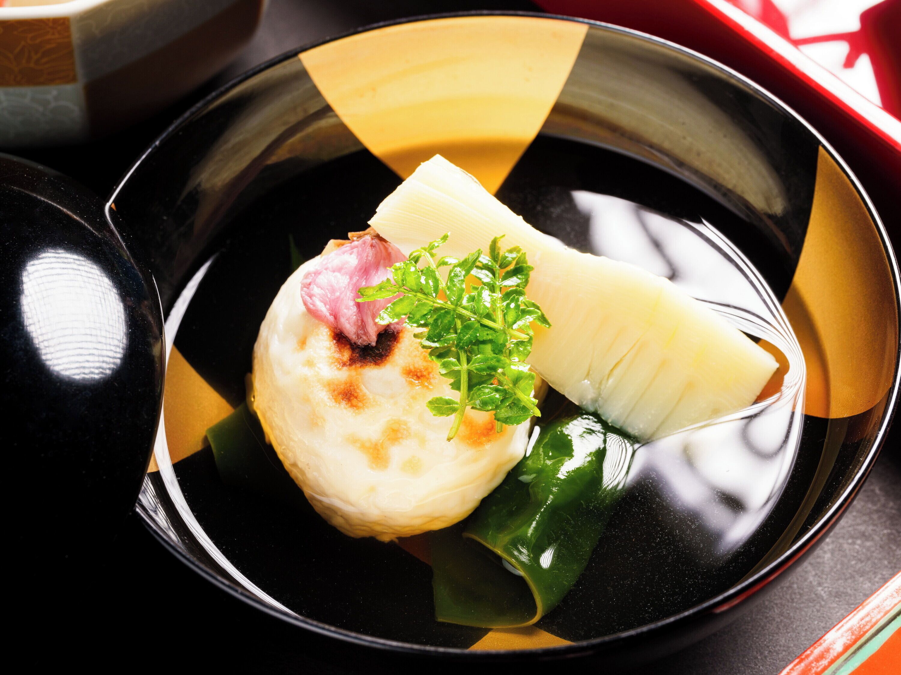 A dish with a piece of meat, a green garnish, and a white item on a black plate with a yellow and black pattern.