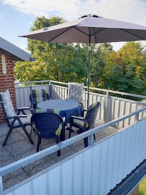 A patio with a table and chairs, an umbrella, and a view of trees and a building. - Apartment 'Plüschmors' with Shared Garden, Balcony and Wi-Fi (Hedwigenkoog)