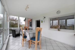 A dining area with a table and chairs, large windows, and a view of the outside. - Apartment 'Plüschmors' with Shared Garden, Balcony and Wi-Fi (Hedwigenkoog)