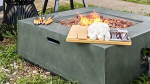 Un foyer extérieur avec des guimauves et les ingrédients nécessaires pour préparer des « s’mores », une chaise et une bouteille de vin, le tout installé devant une maison.