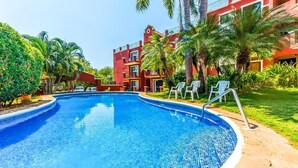 A swimming pool with a tiled edge, surrounded by palm trees and a red building with balconies.