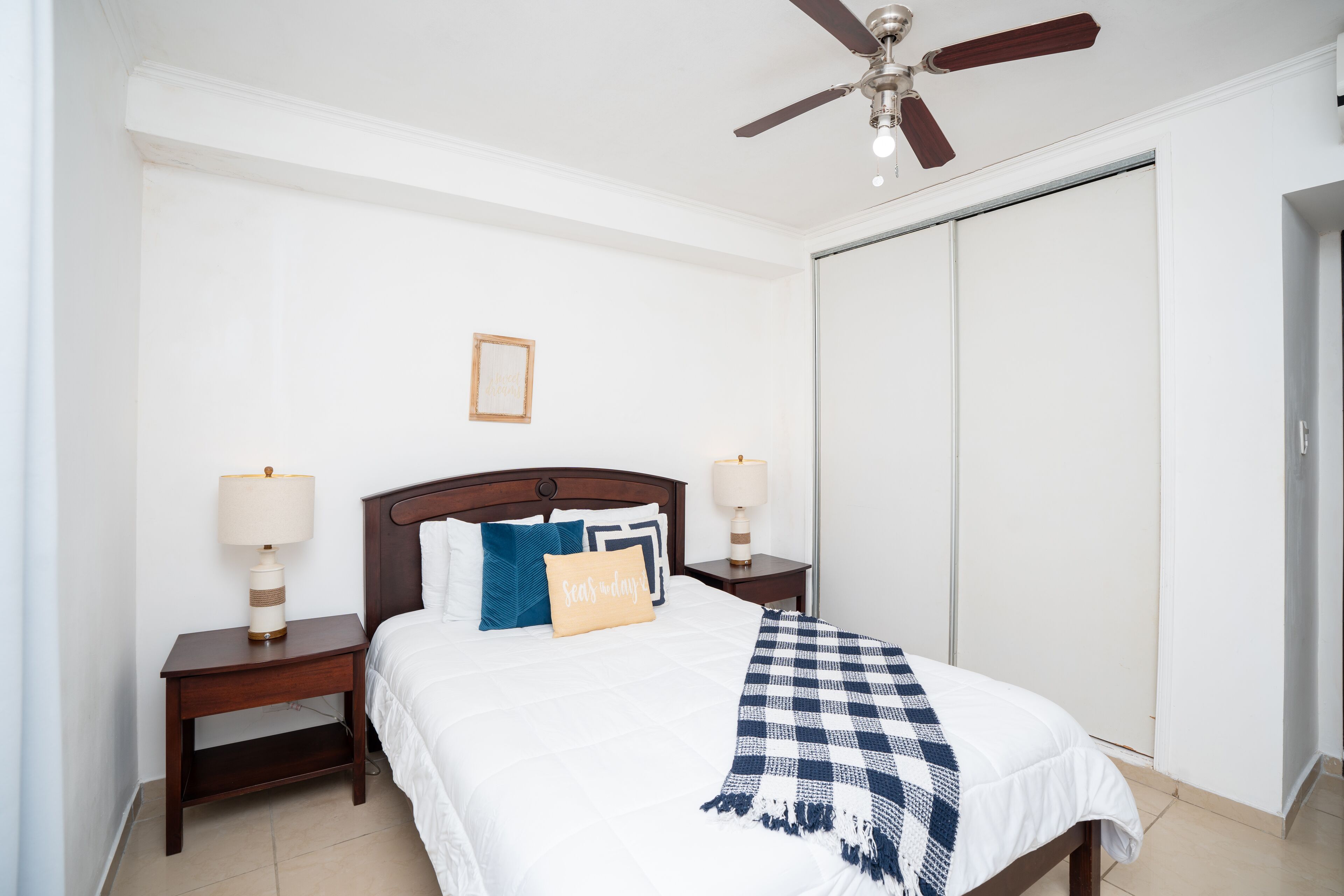 A neatly arranged bedroom with a bed, two bedside tables with lamps, a ceiling fan, and a wardrobe.