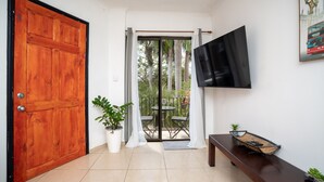A room with a wooden door, a television mounted on the wall, a potted plant, and a bench.
