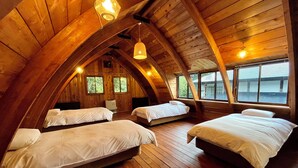 Une chambre confortable située sous les toits, avec des poutres apparentes, trois lits et de grandes fenêtres.