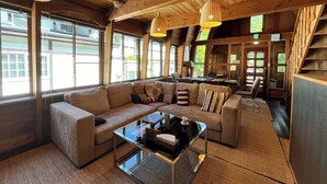 Un salon chaleureux avec un canapé d’angle, une table basse en verre et des poutres en bois au plafond.