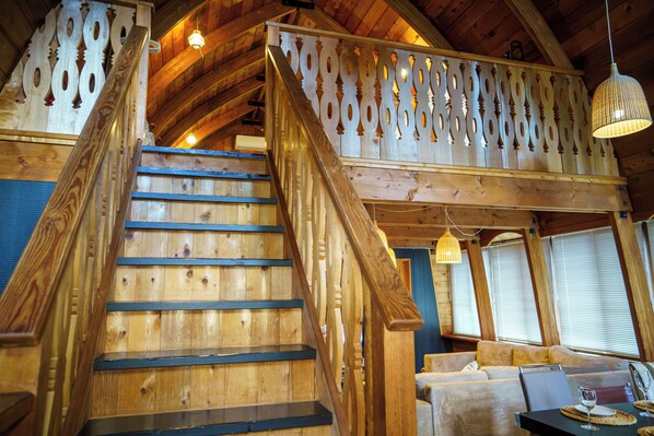 A wooden staircase with a railing leading to a balcony with decorative cutouts. - Hakuba Mountain Cabin (Hakuba)