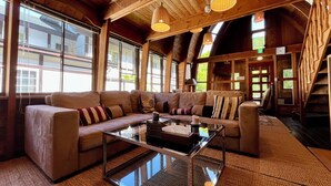 Un vaste espace de vie comprenant un grand canapé, une table basse en verre et des poutres en bois au plafond.