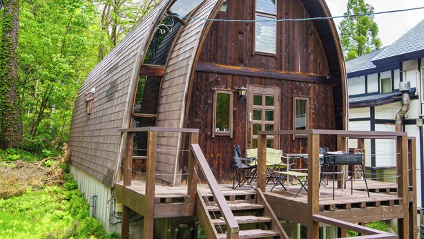 Une cabane en bois dotée d’une terrasse, d’un escalier et d’un petit espace extérieur aménagé pour s’asseoir.