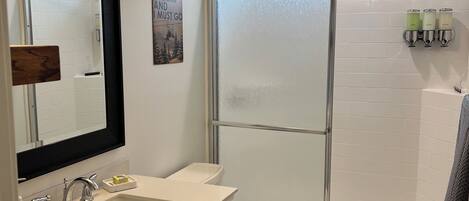 Ein modernes Badezimmer mit Waschbecken, Waschtisch und Toilette. Es verfügt über eine Dusche mit Glastrennwand und ein Fenster für natürliches Licht.