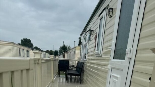 A covered wooden deck with a white railing, leading to a building with a white door and windows.