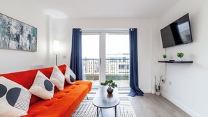 Uma sala de estar moderna com um sofá vermelho, uma televisão de tela plana, uma mesa de centro com um bonsai e uma varanda com cortinas azuis.