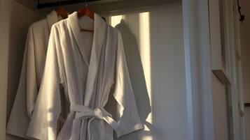 A white robe hanging on a wooden hanger in a room with white walls and a window.