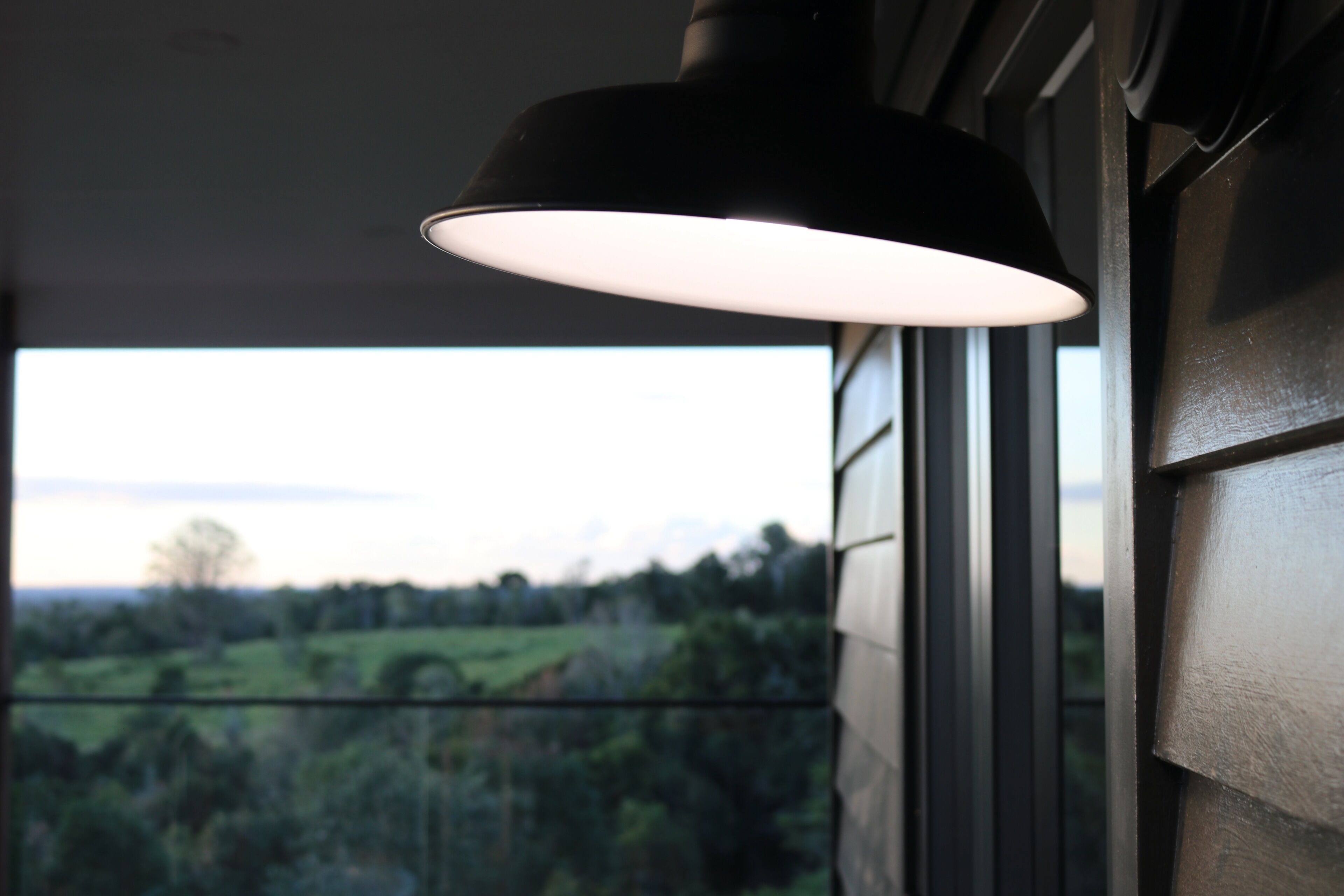 A black pendant lamp hanging near a window with a view of a green landscape.