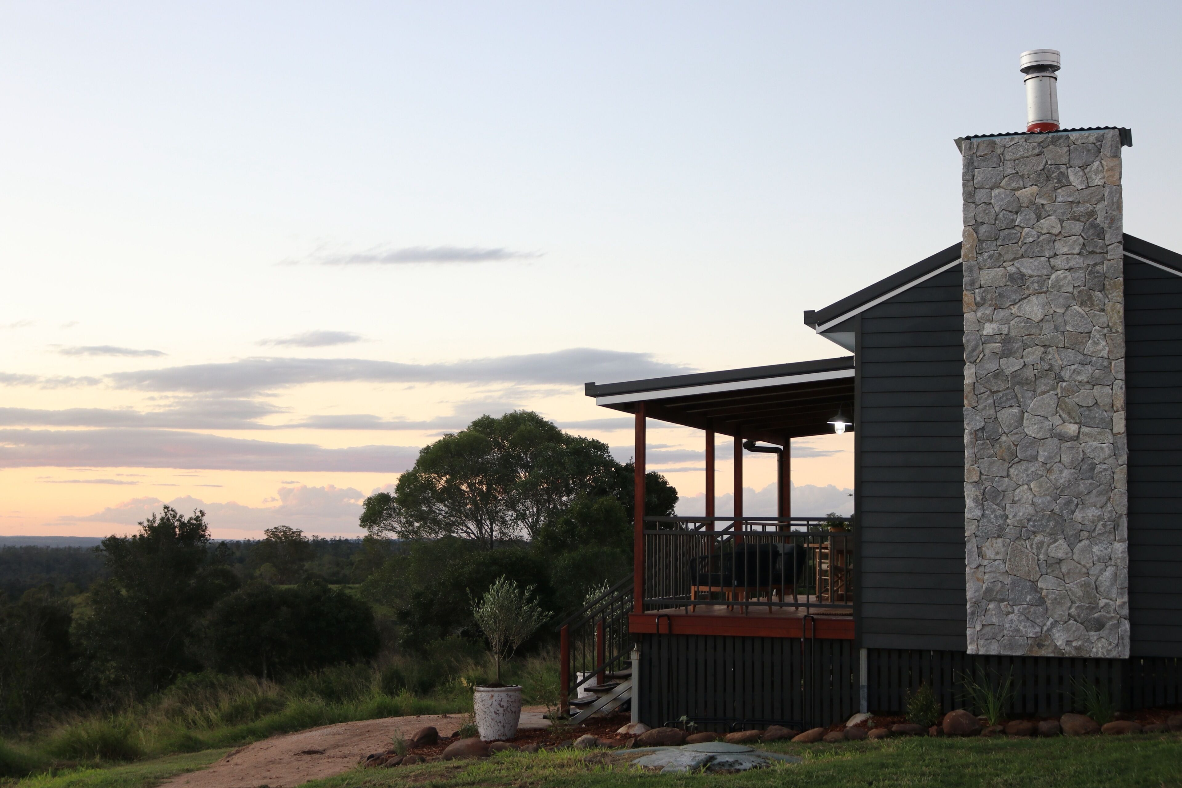 A modern house with a stone chimney, a covered porch, and a view of the surrounding landscape.