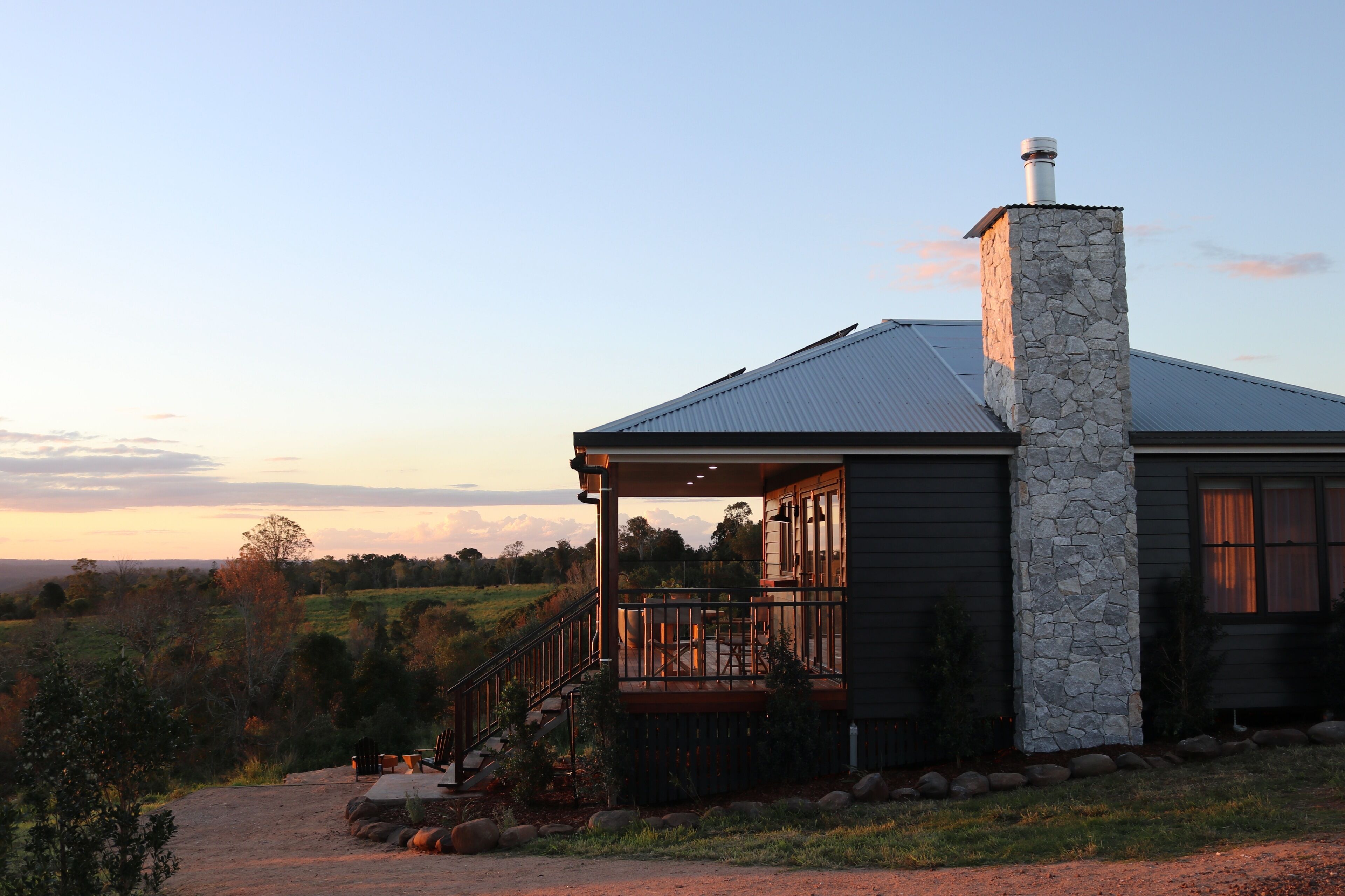 A house with a stone chimney, a porch with a railing, and a view of the countryside.