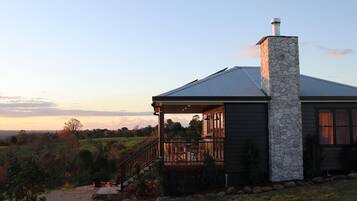 A house with a stone chimney, a porch with a railing, and a view of the countryside.