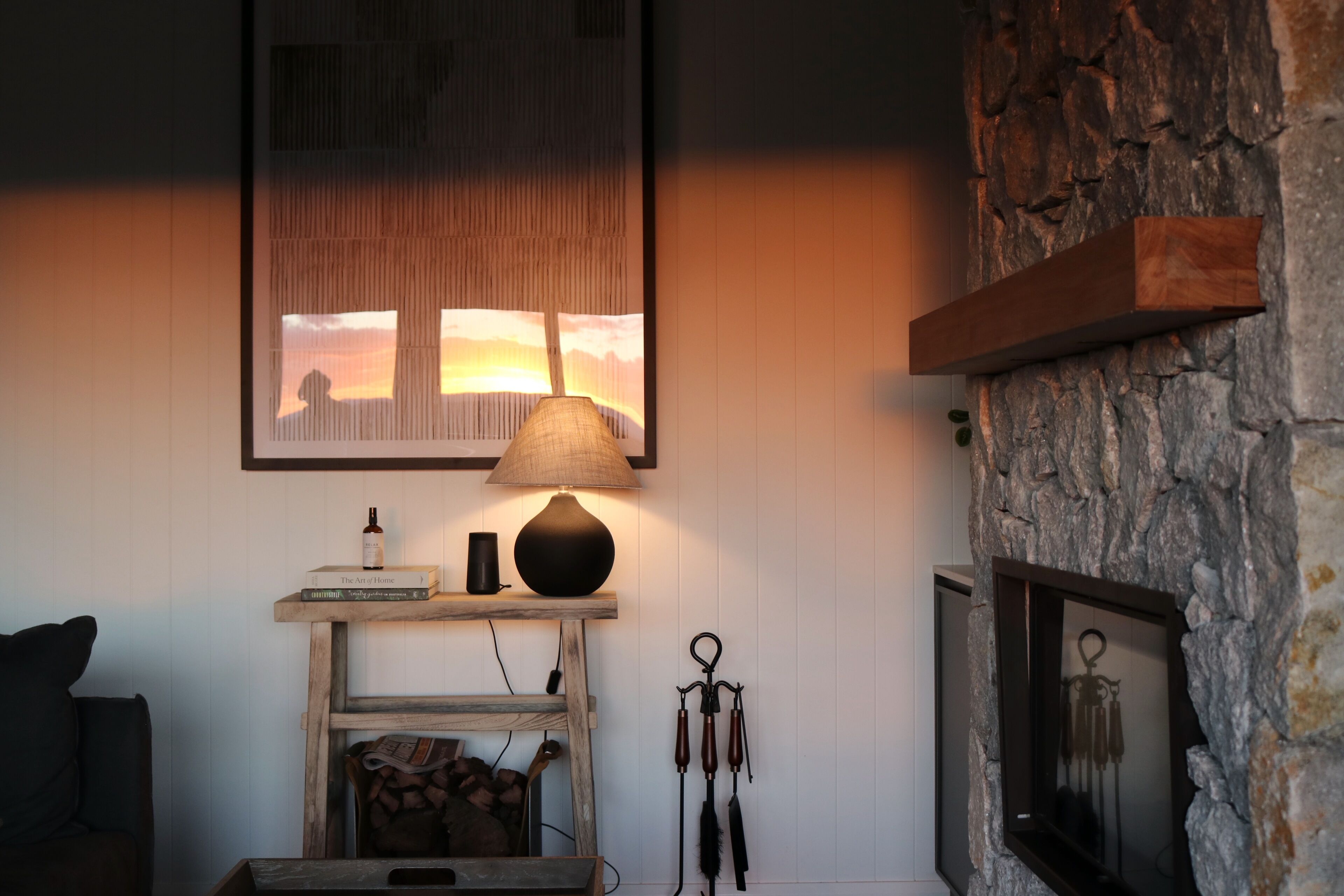 A cozy living room with a fireplace, a lamp, a framed picture, and a shelf with books and a bottle.