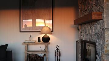 A cozy living room with a fireplace, a lamp, a framed picture, and a shelf with books and a bottle.