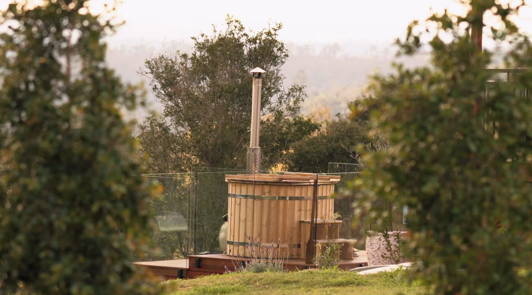 A sauna structure with a chimney, surrounded by greenery.