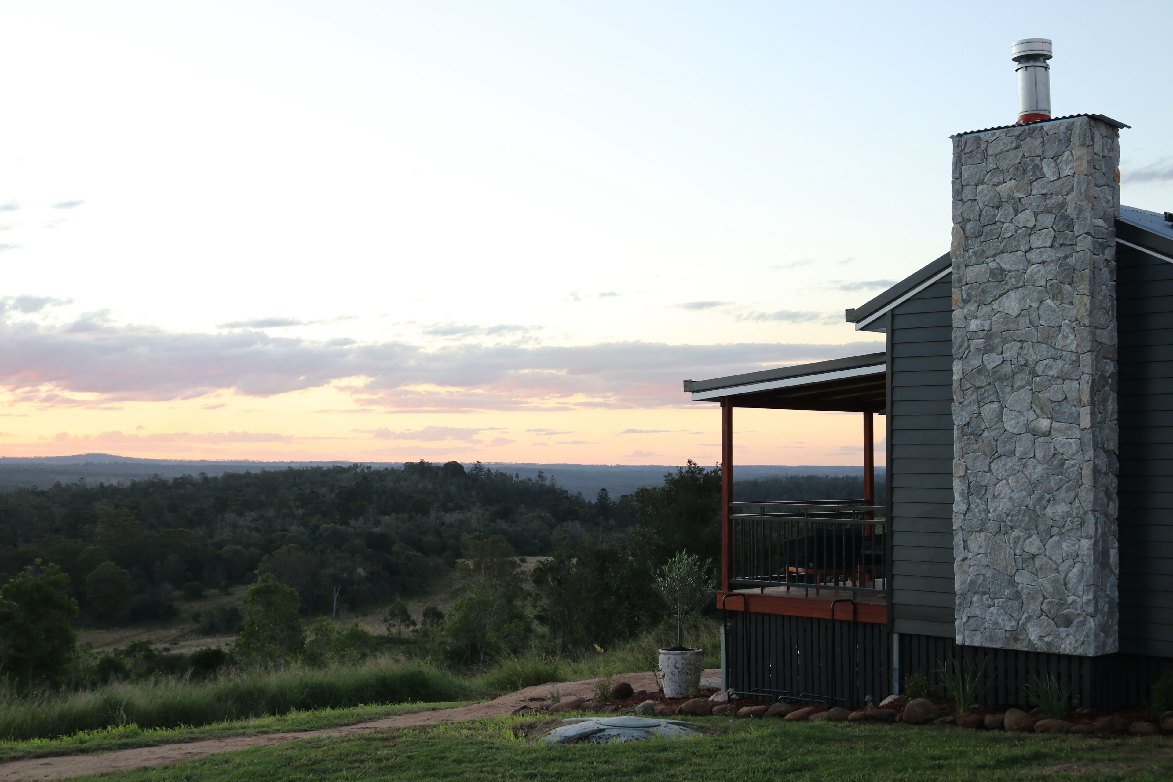 Une maison moderne avec une cheminée en pierre, un balcon et une vue sur un paysage boisé.