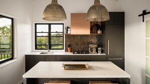 Une cuisine moderne dotée d’un grand îlot central, de luminaires suspendus et offrant une vue sur la verdure environnante.
