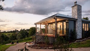 Une maison moderne avec une cheminée en pierre, un porche abrité et une vue sur le paysage environnant.