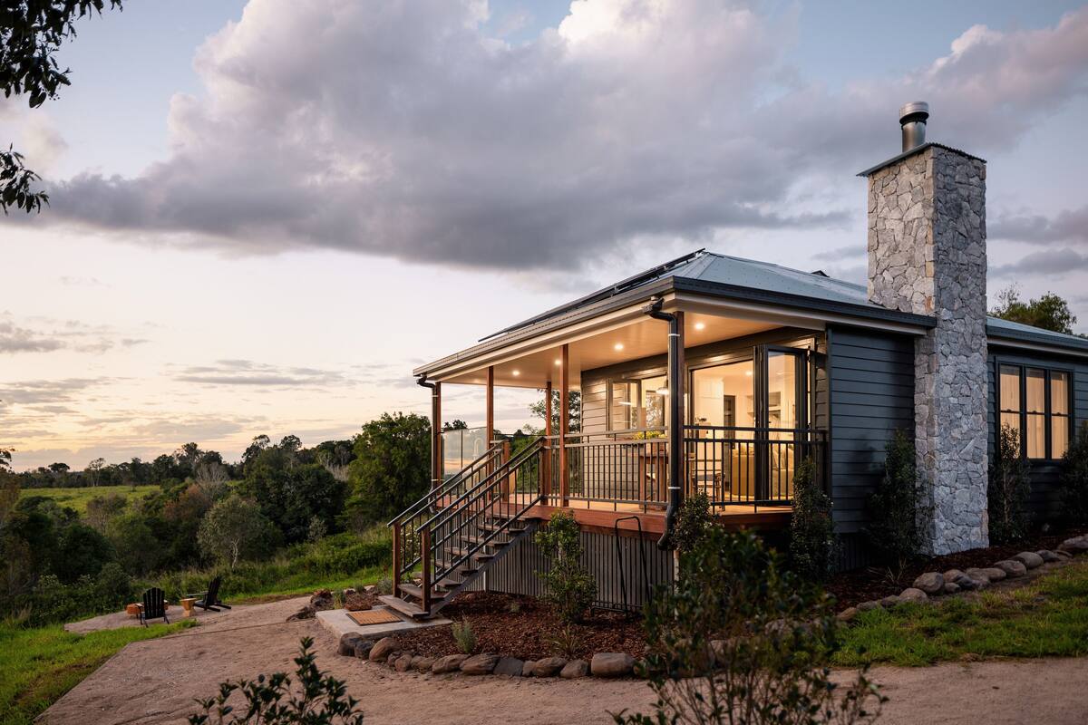 Une maison moderne avec une cheminée en pierre, un porche abrité et une vue sur le paysage environnant.