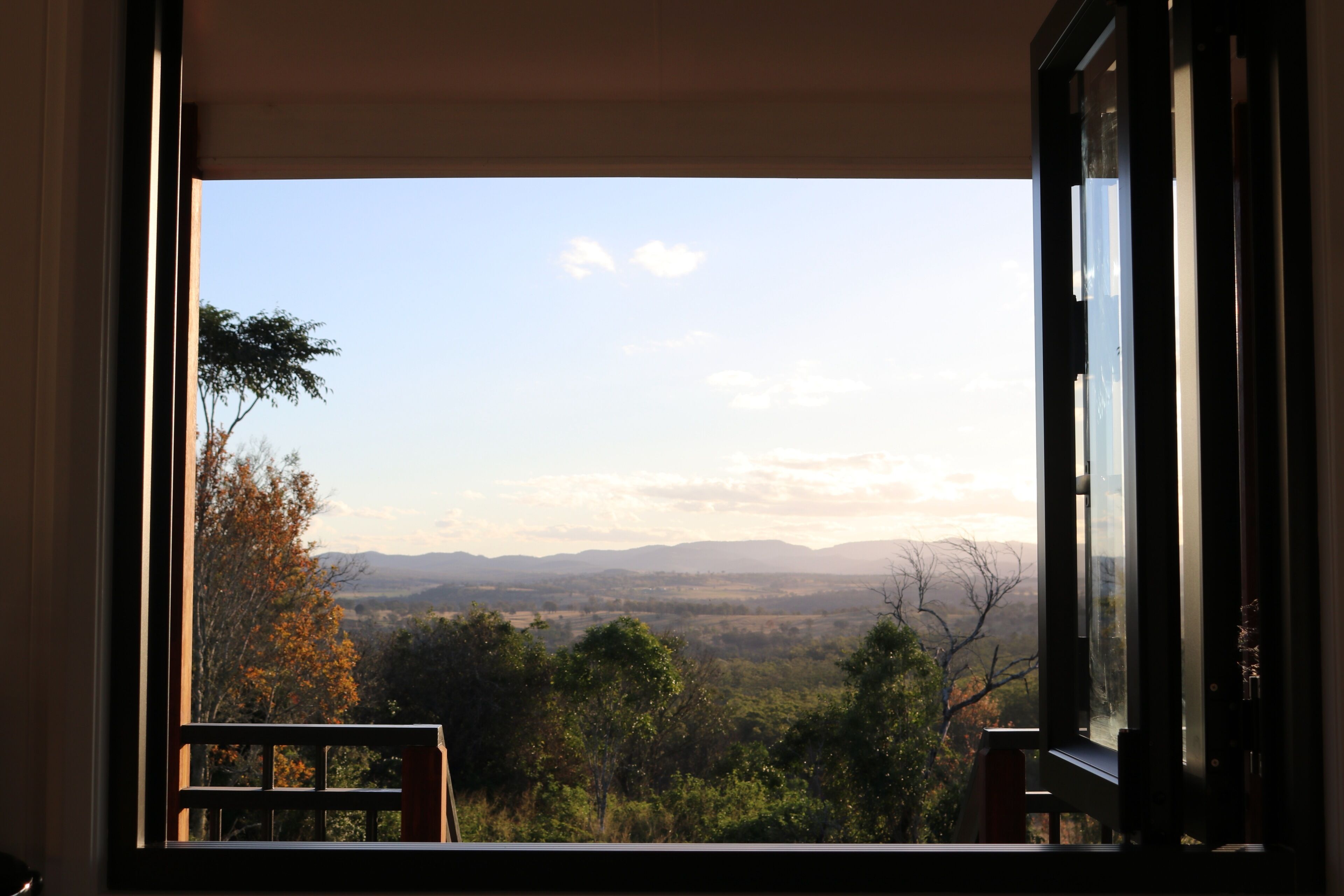 A window with a view of a landscape including trees and distant hills.