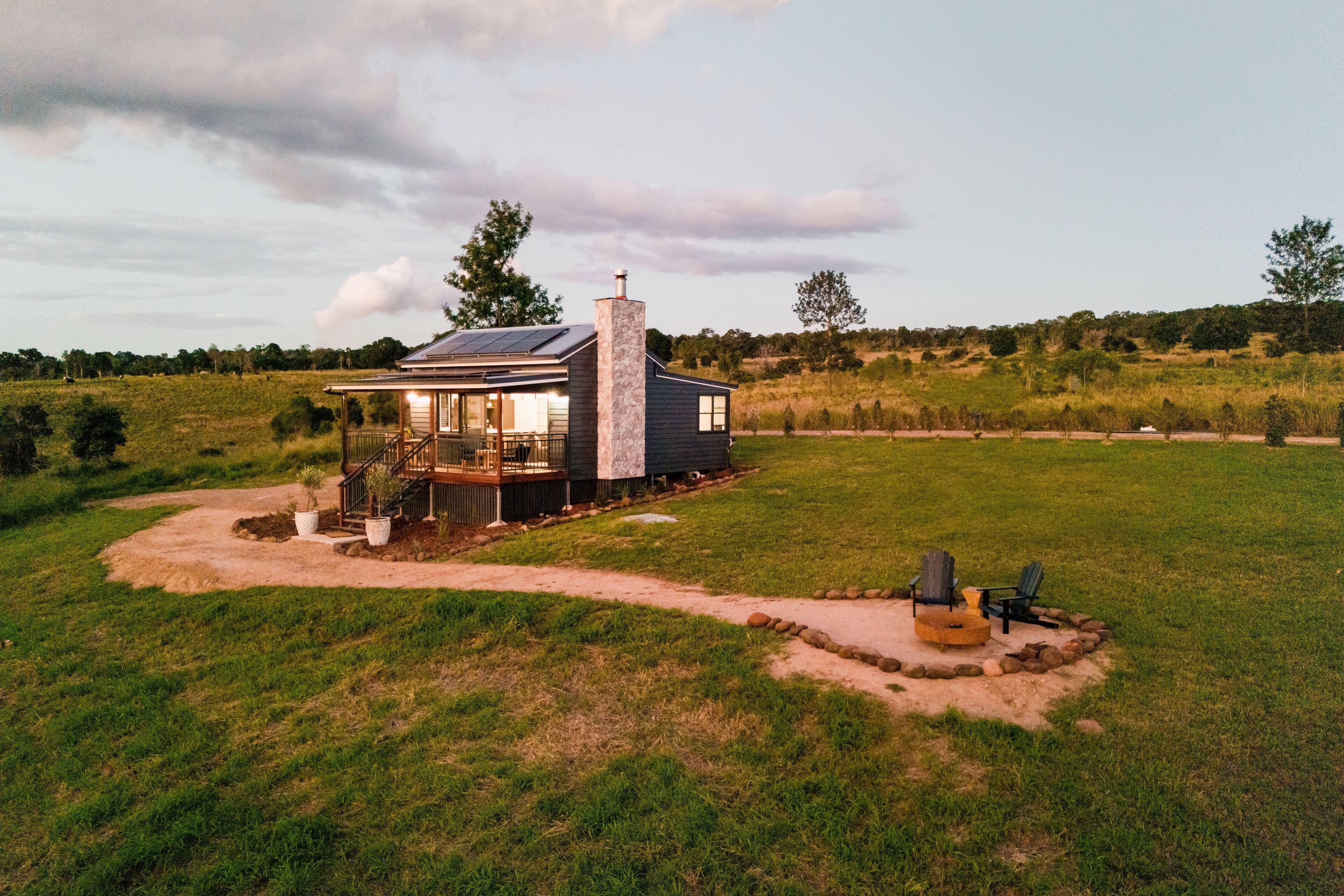 A modern house with a large deck, surrounded by a grassy field and trees.