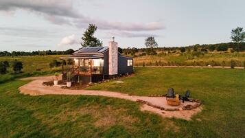 A modern house with a large deck, surrounded by a grassy field and trees.