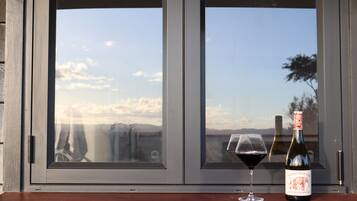 Une bouteille de vin et un verre posés sur une surface en bois, devant une fenêtre donnant sur le ciel et un paysage lointain.