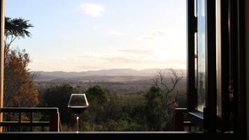 A view from a window with a glass of wine, overlooking a landscape with trees and distant hills.