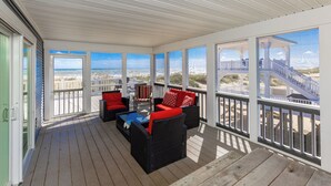 A covered outdoor area with wicker furniture and red cushions, overlooking a beach and a staircase. - Staud's Stilts - Oceanfront home w/pool and direct beach access (Virginia Beach)