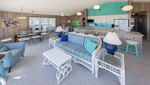 A modern living room with a sofa, dining area, and kitchen. - Staud's Stilts - Oceanfront home w/pool and direct beach access (Virginia Beach)