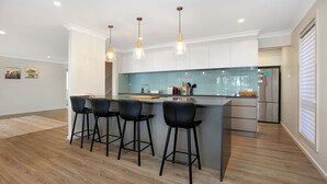 Una cocina moderna con una isla central, taburetes de bar, iluminación colgante y un refrigerador de acero inoxidable.