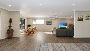 Amplia sala de estar con un sofá gris, una zona de comedor con sillas de mimbre y un gran ventanal con persianas.