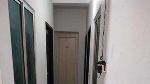 A narrow hallway with white walls, a tiled floor, and two red carpets leading to a door at the end. - Eben Service Apartment  (Chennai)