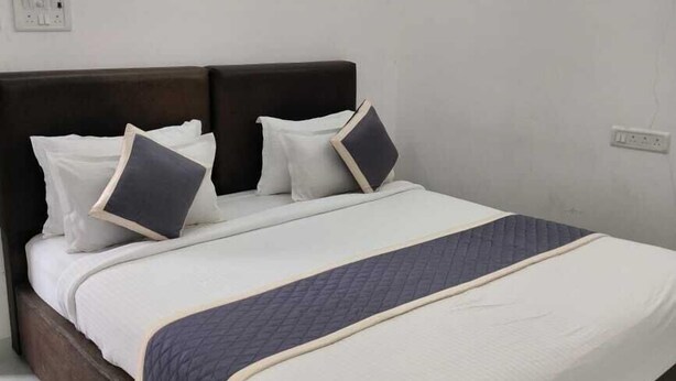 A neatly made bed with a dark headboard, white bedding, and a quilted blanket. - Eben Service Apartment  (Chennai)